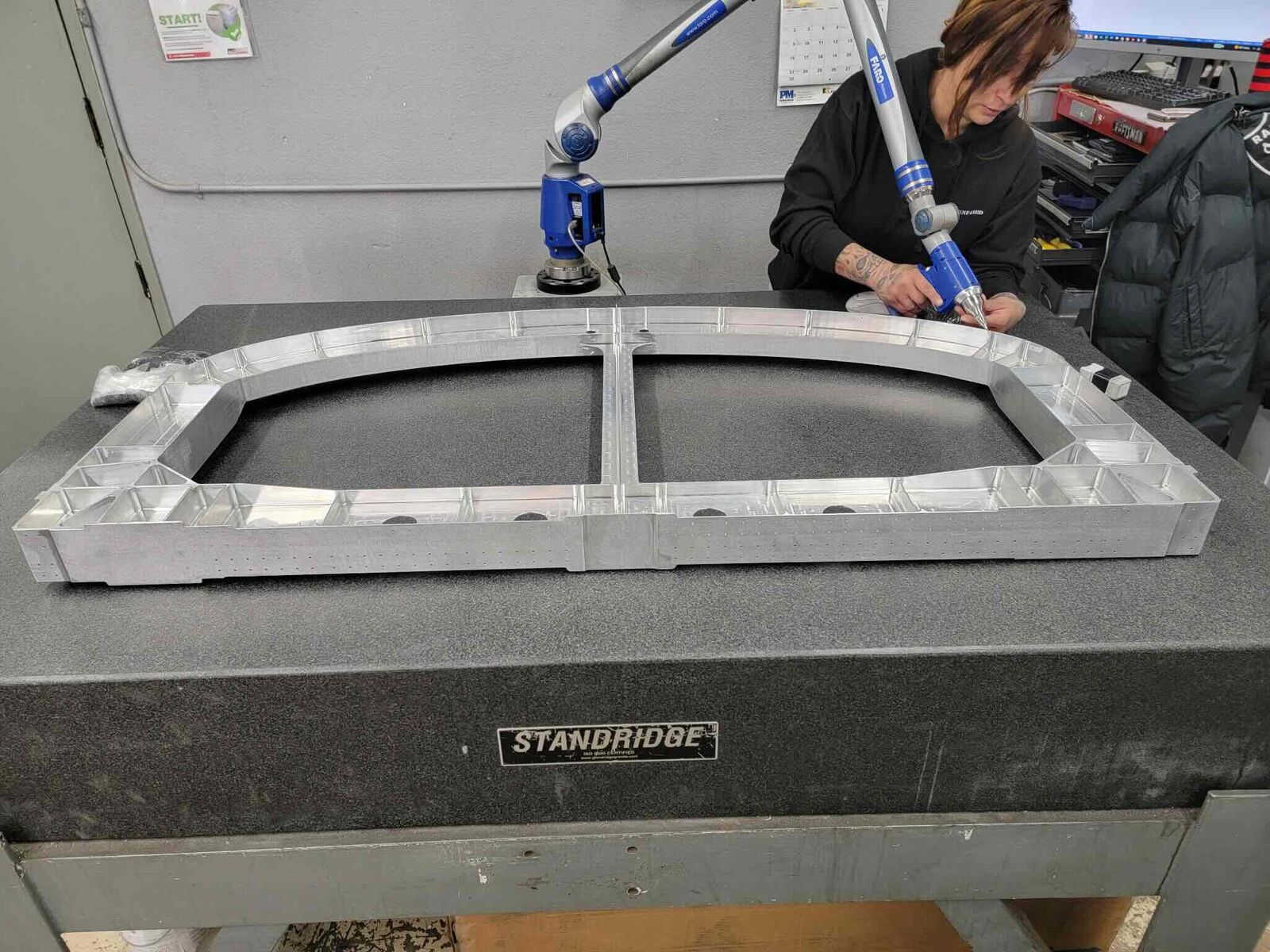 Machined aluminum frame being measured with a portable CMM arm on a granite table