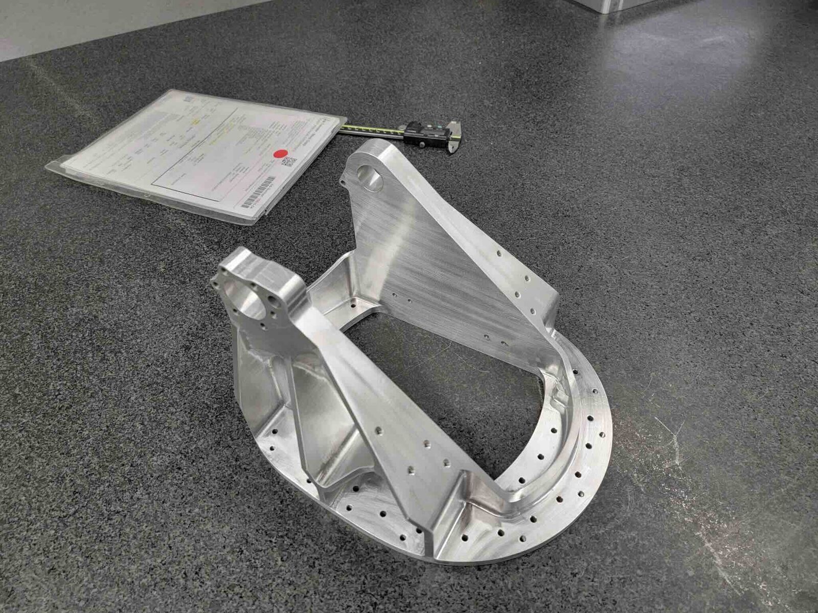 Complex aluminum bracket beside its inspection report