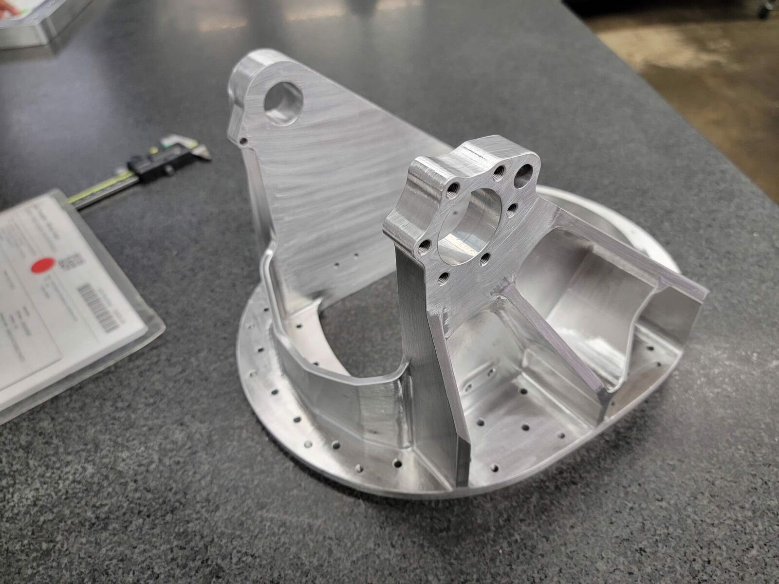 Complex machined aluminum bracket next to calipers